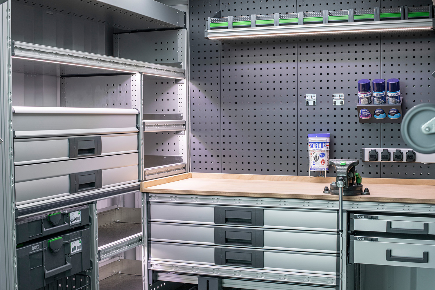 Vue intérieure d'un atelier en container avec aménagement de véhicule bott vario 3, y compris des étagères, des tiroirs et un banc de travail.